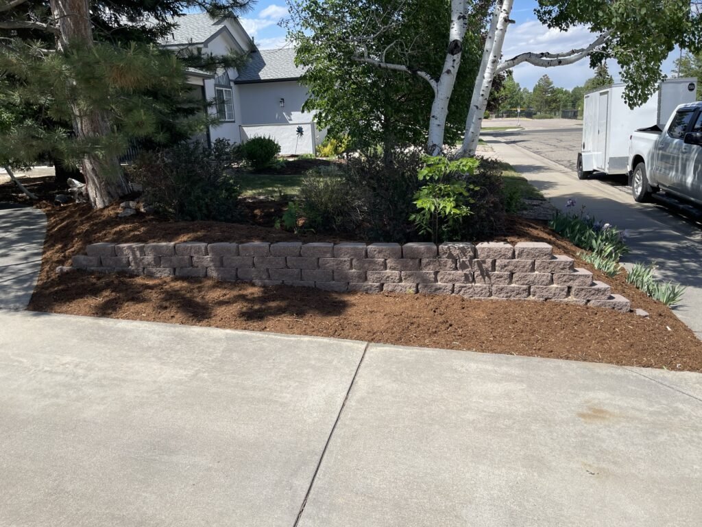Fresh premium brown mulch professionally installed throughout a large landscape bed near a brick wall in Johnstown CO.