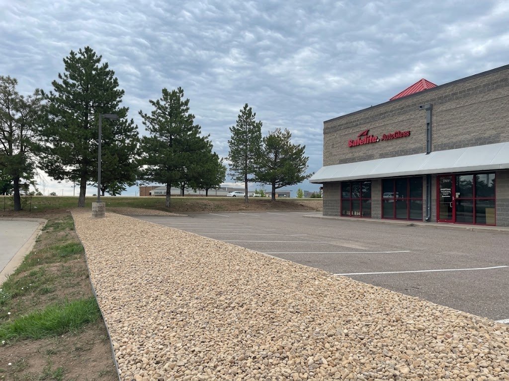 Finished commercial landscaping featuring clean beige river rock beds and pine tree landscaping alongside a commercial parking lot in Northern Colorado.