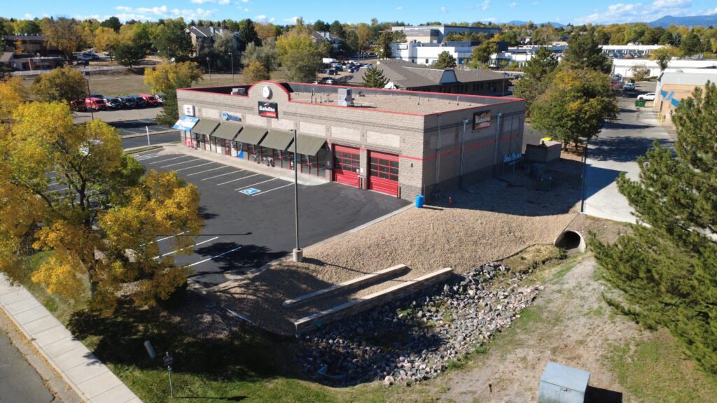 Aerial drone view of commercial landscaping project in Northern Colorado featuring river rock gravel installation, multi-tiered retaining walls, and drainage channel.